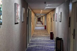 A hotel hallway with framed artwork on the walls, a carpeted floor, and doors on the right.