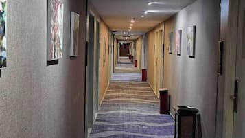 A hotel corridor with framed artwork on the walls, a patterned carpet, and a row of doors on the right.
