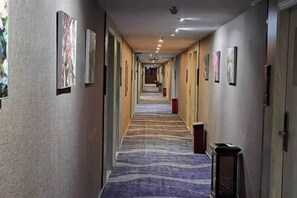 Een hotelgang met ingekaderde kunstwerken aan de muur, een kamerbreed tapijt en een rij deuren aan de rechterkant.