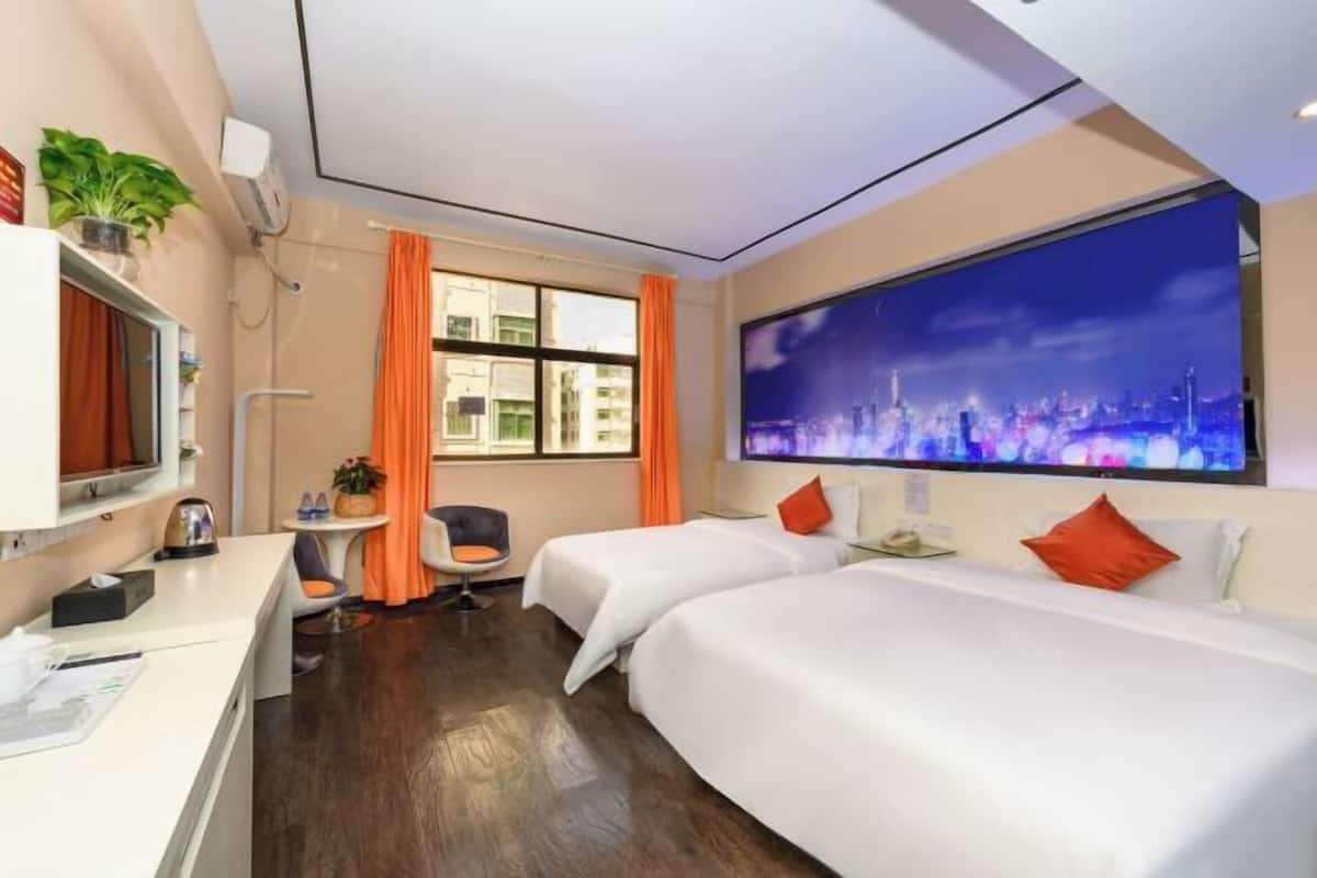 A hotel room with two beds, a desk, a chair, a TV, and a cityscape view.