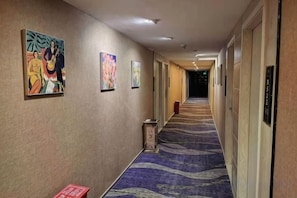 A hotel hallway with artwork on the walls, a carpeted floor, and doors on the right. - Quanzi Art Inn (Shenzhen)