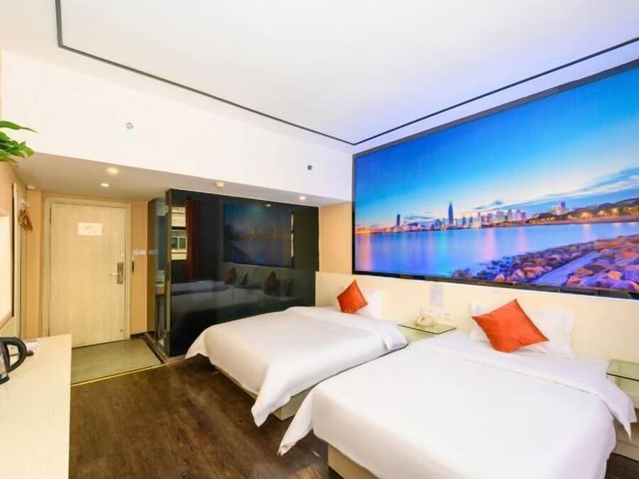 Quarto de hotel com duas camas, uma pintura grande da paisagem urbana na parede, uma escrivaninha com chaleira e uma planta em vaso.