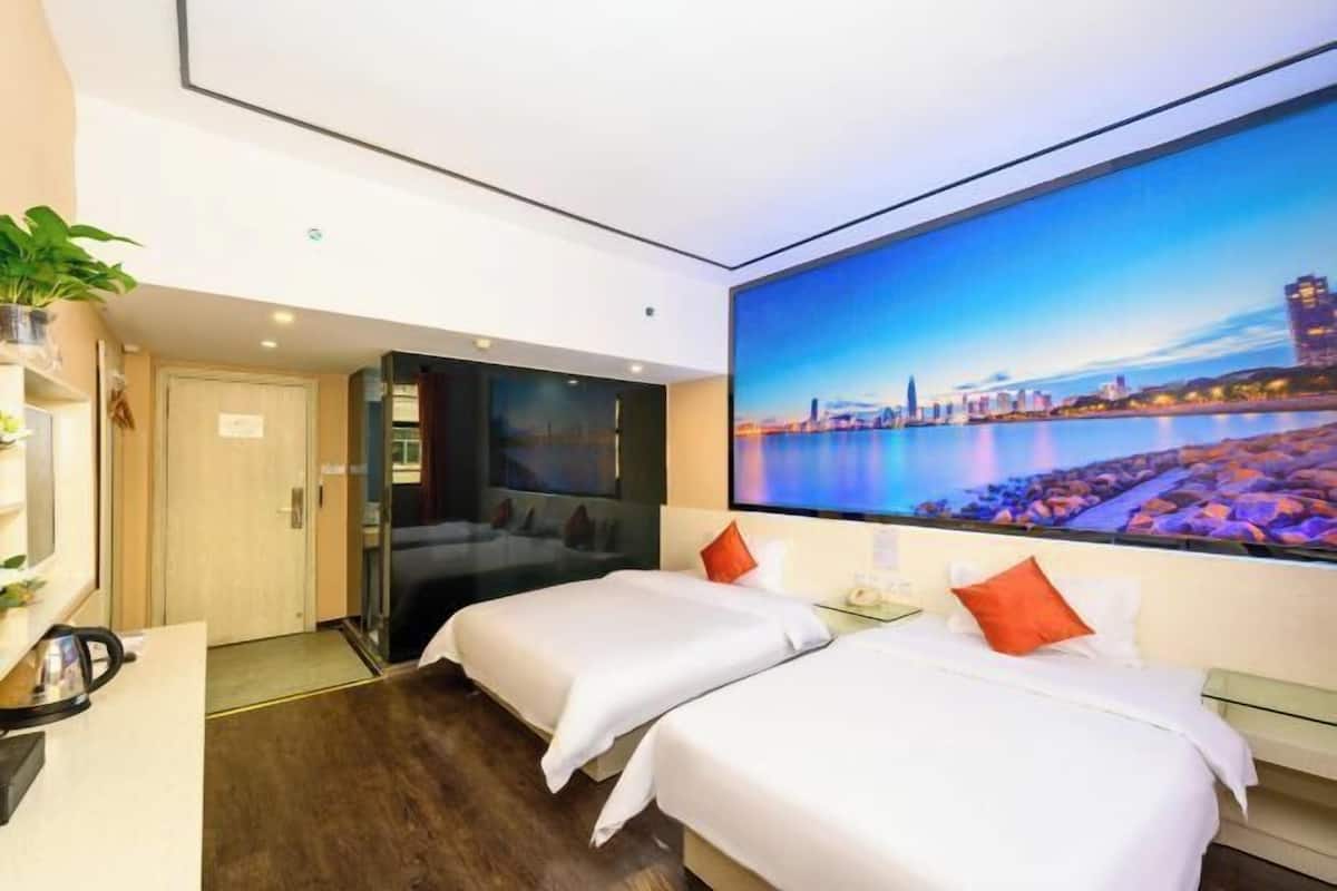 A hotel room with two beds, a desk, a TV, and a cityscape view.