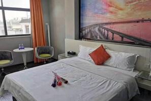 A hotel room with a large bed, a nightstand, a chair, a small table, and a window with curtains. - Quanzi Art Inn (Shenzhen)