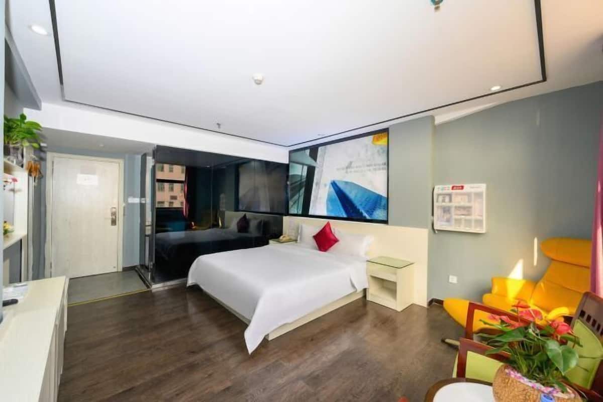 A modern hotel room with a large bed, a desk, a chair, and a TV.