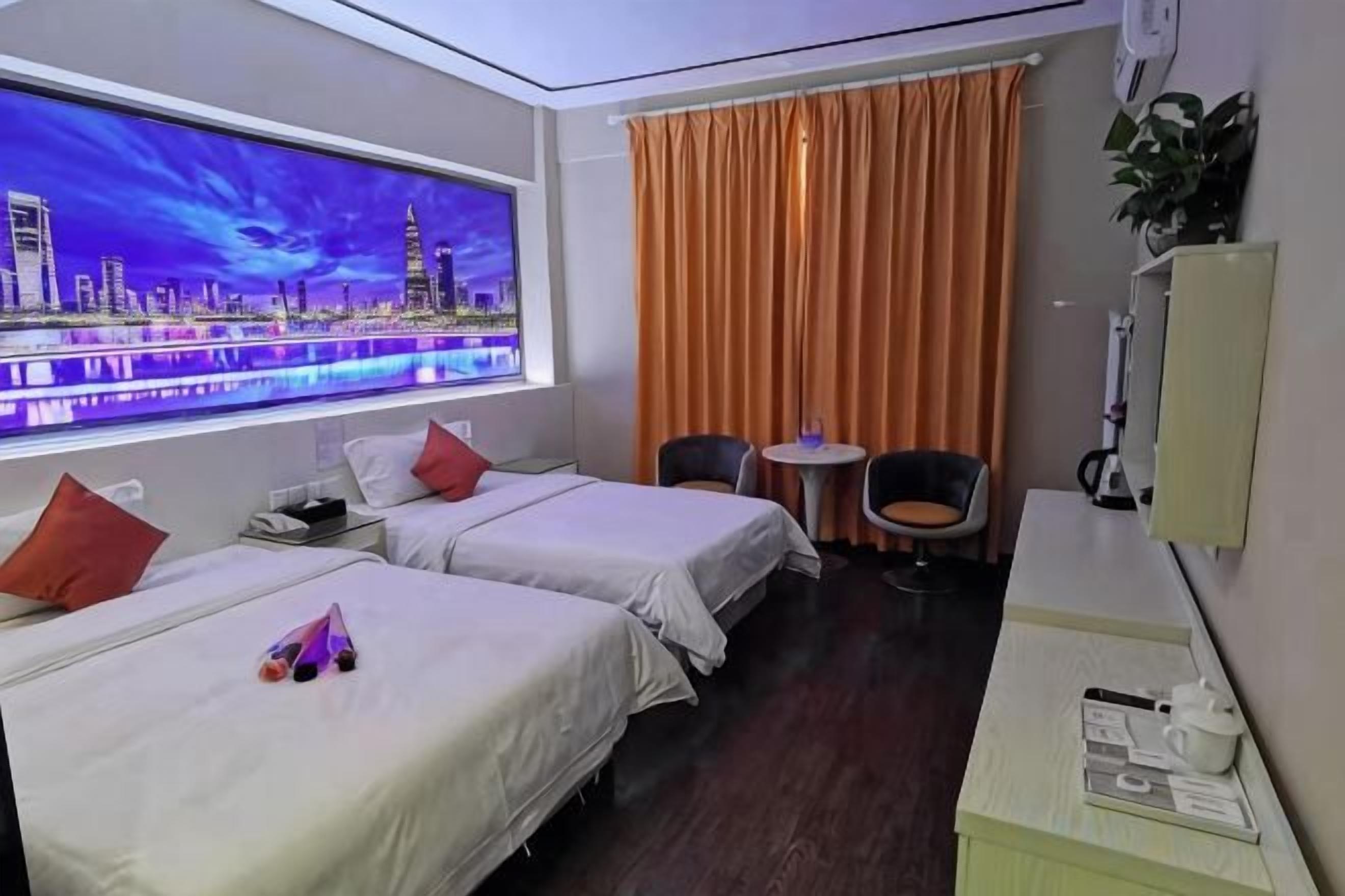 A hotel room with two beds, a window with a cityscape view, a desk with a chair, and a small table with a plant.