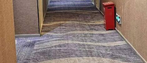 A carpeted hallway with a trash bin and a sign on the wall.