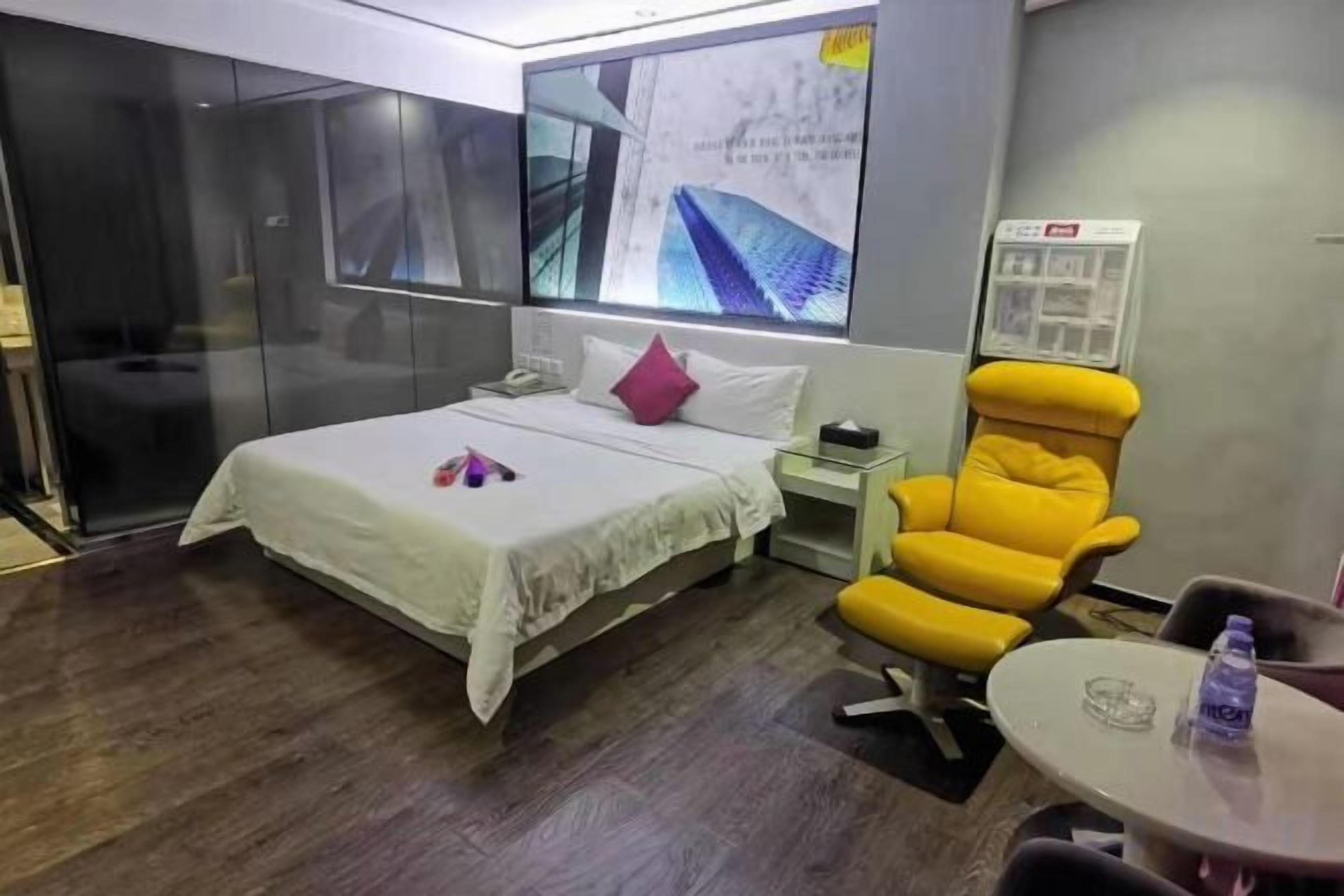 A hotel room with a bed, a chair, a small table, and a wall-mounted screen.