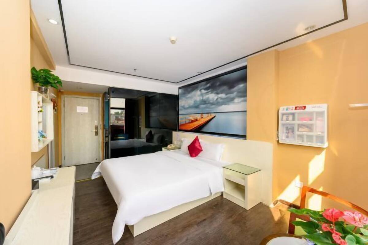 A modern hotel room with a bed, bedside table, and a large window.