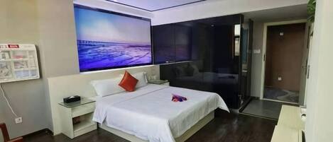 A modern bedroom with a large bed, bedside tables, a nightstand, a wall-mounted TV, and a door leading to another room.