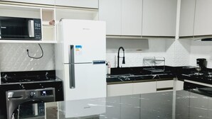 A modern kitchen with white cabinets, a black countertop, a white refrigerator, a microwave, and a dishwasher.