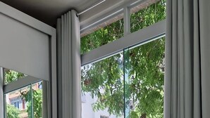 A hotel room with two beds, a large window with curtains, and a view of buildings and trees.
