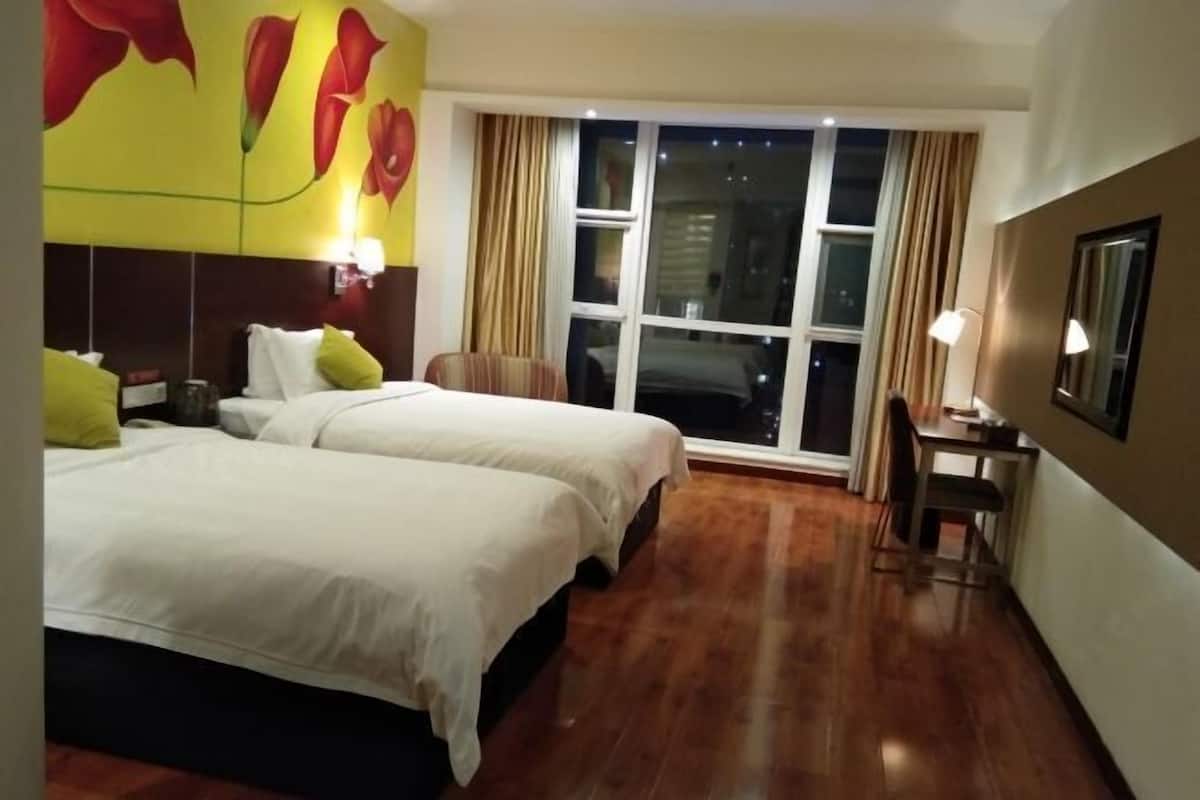A hotel room with two beds, a desk, a chair, and a large window with curtains.