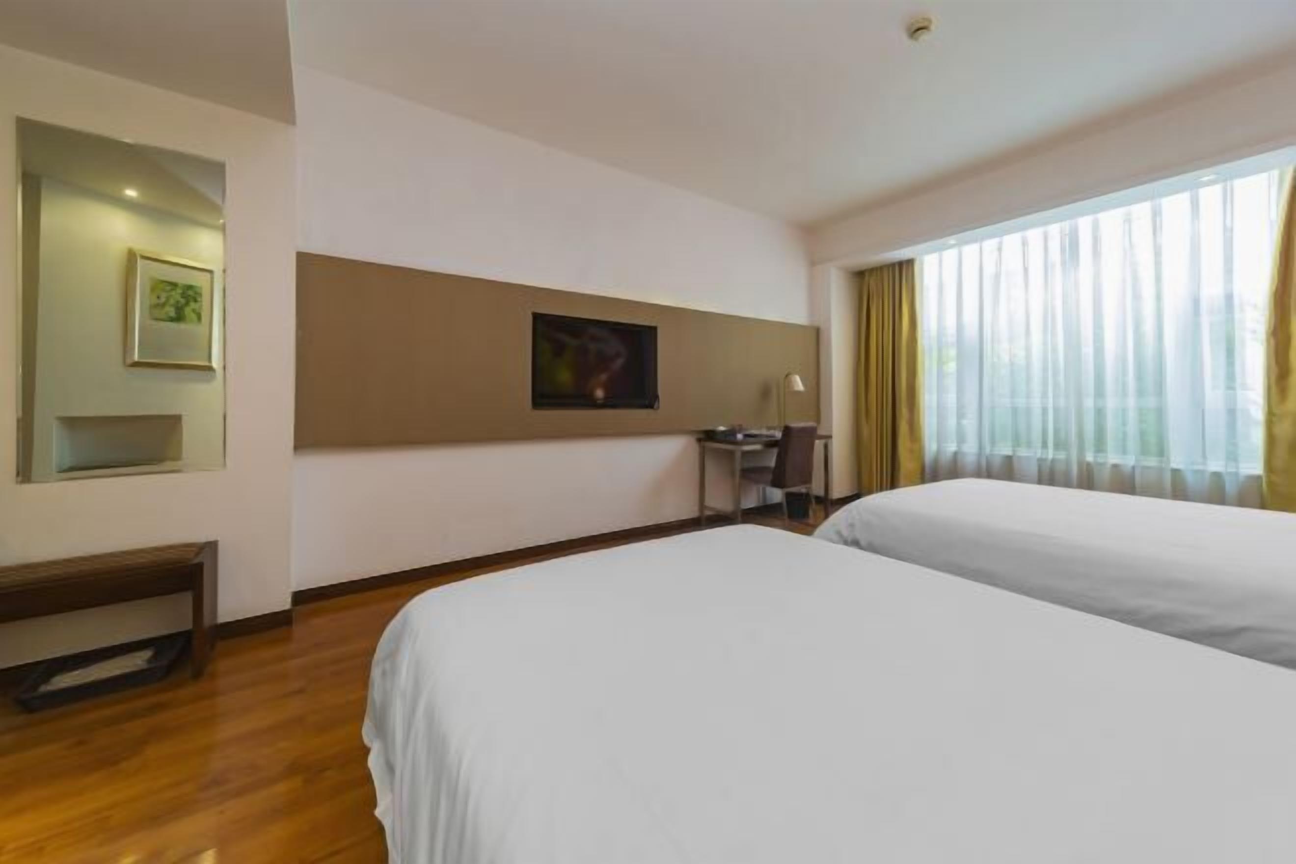 Une chambre d’hôtel avec deux lits, un bureau, une chaise et une grande fenêtre avec des rideaux.