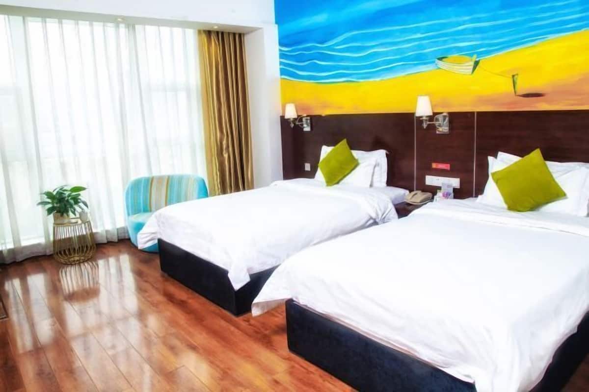 A hotel room with two beds, a large window with curtains, a plant, and a colorful mural on the wall.