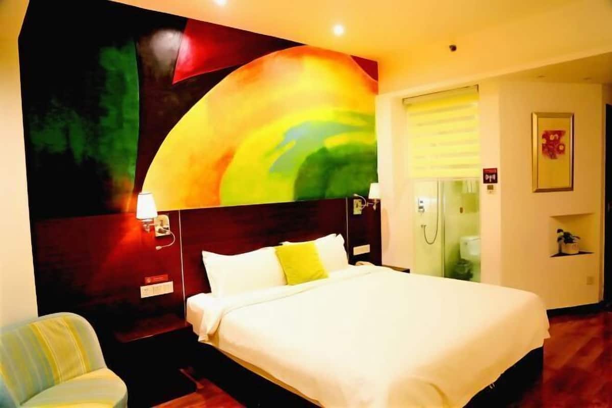 A hotel room with a large bed, a nightstand, a chair, and a wall mural.