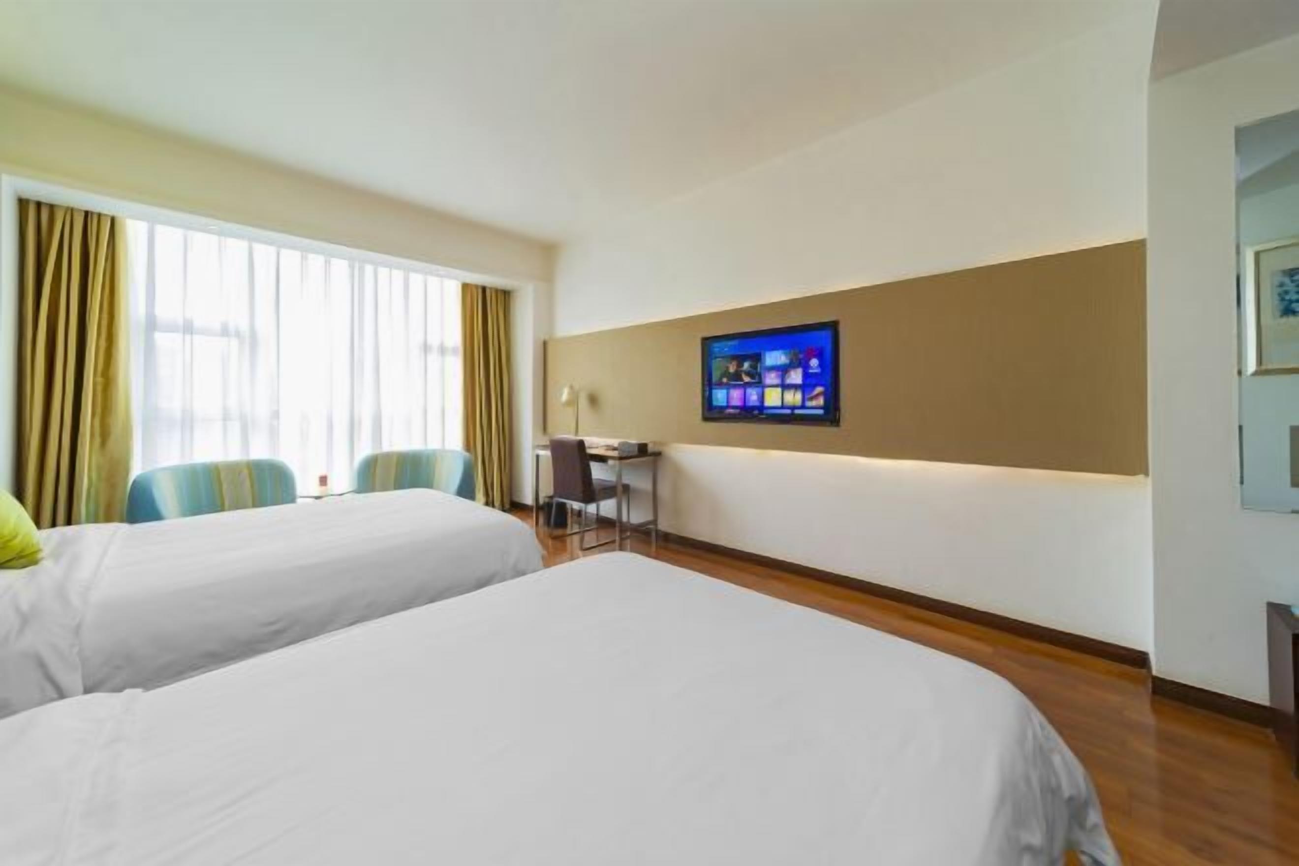 A hotel room with two beds, a desk, a chair, and a TV on the wall.