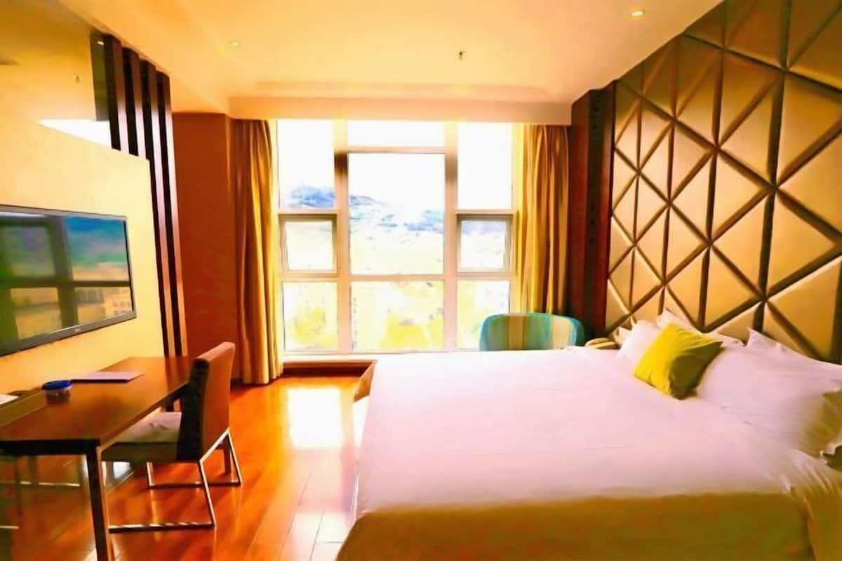 A hotel room with a bed, a desk, a chair, and a TV.