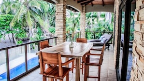 A wooden dining table with chairs, a glass vase, and a view of a pool and tropical vegetation.