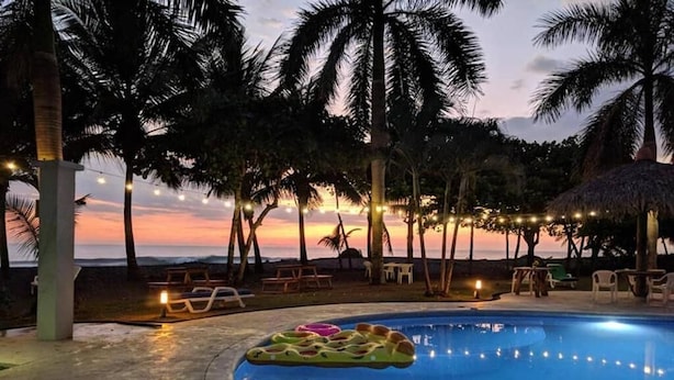 A swimming pool with lounge chairs and palm trees, surrounded by string lights.
