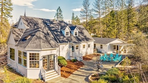 A two-story house with a wrap-around porch, a small detached garage, and a backyard with a swimming pool and outdoor seating.