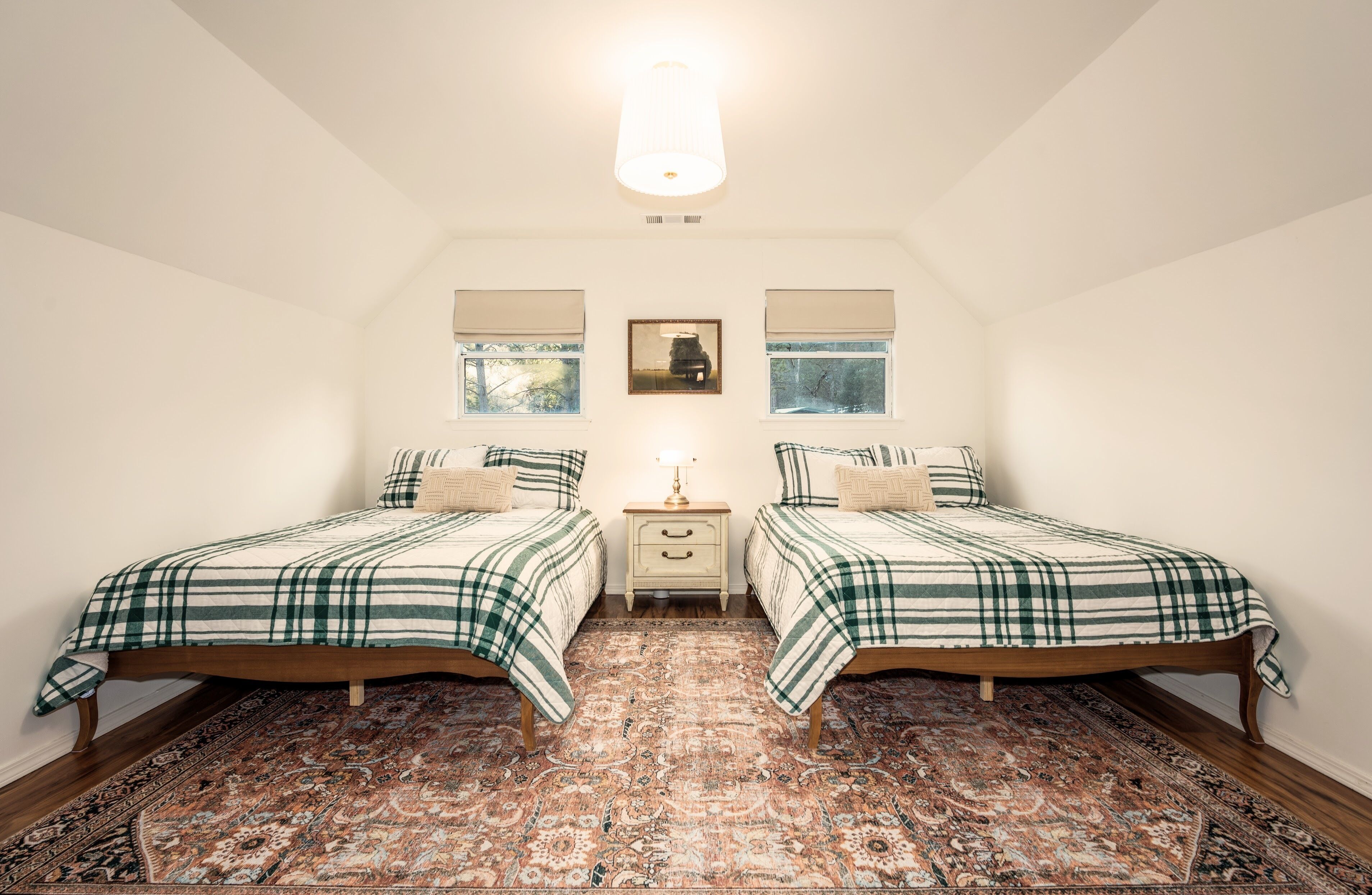A bedroom with two beds, a nightstand, a lamp, and a patterned rug.