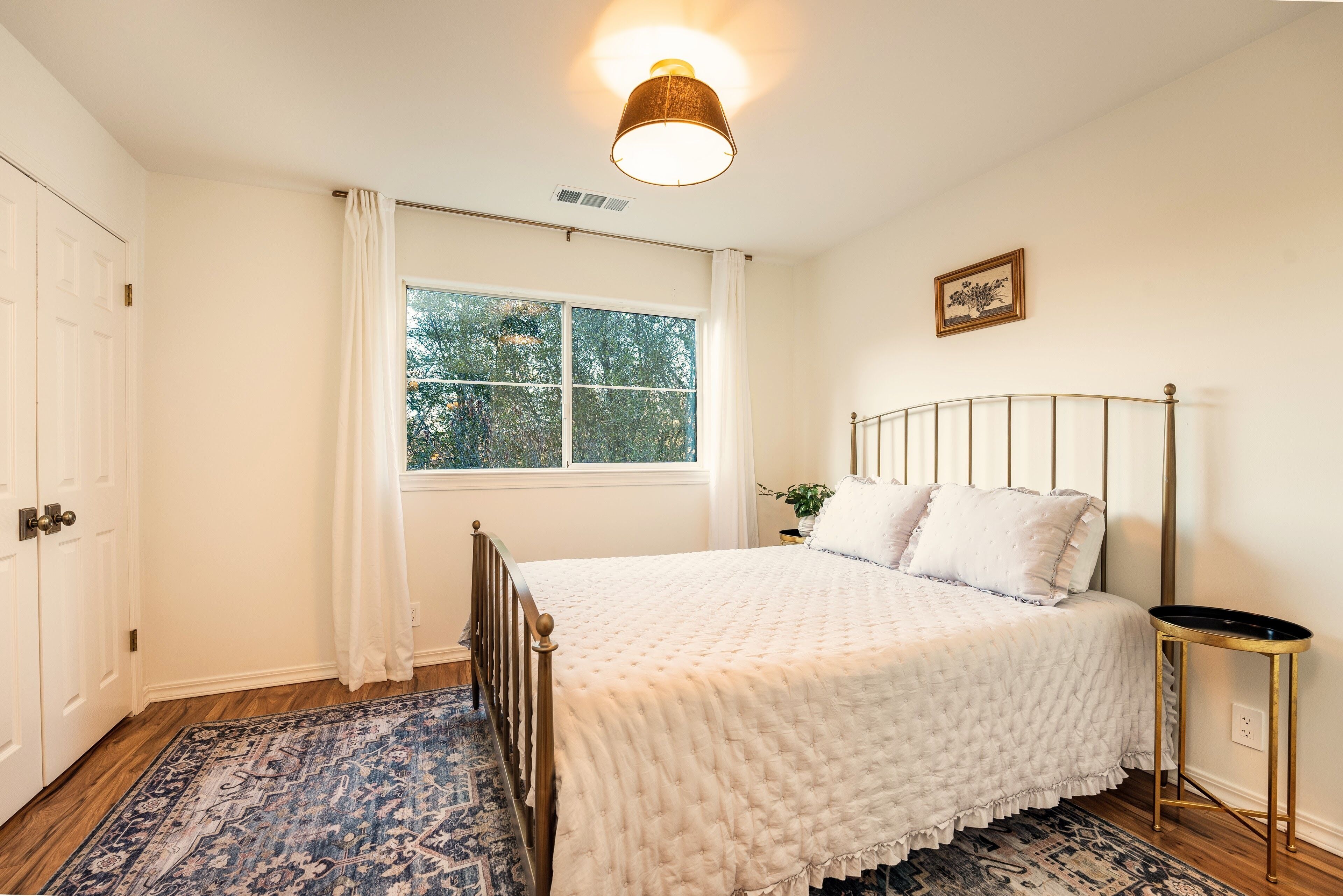 A bedroom with a bed, a window with curtains, a bedside table, and a rug.