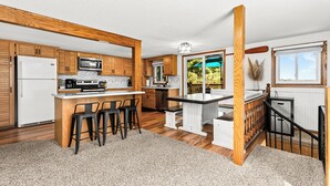A modern kitchen with wooden cabinets, a central island with bar stools, a microwave, and a refrigerator. - Lakefront Cabin, Hot Tub, Sauna, Fireplace, Game Room, Near Duluth  (Saginaw)