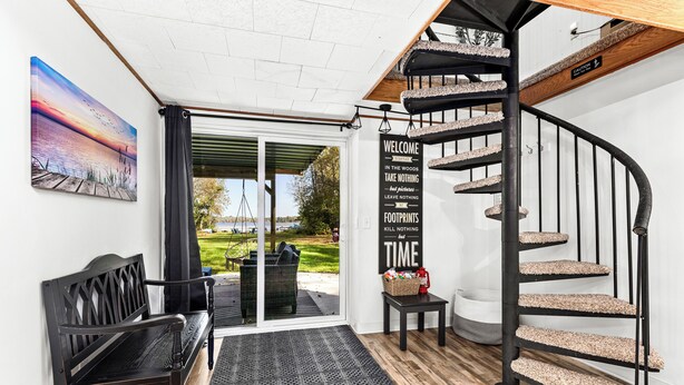 A modern interior with a black spiral staircase, a bench, a welcome sign, and a view of the outdoors. - Lakefront Cabin, Hot Tub, Sauna, Fireplace, Game Room, Near Duluth  (Saginaw)