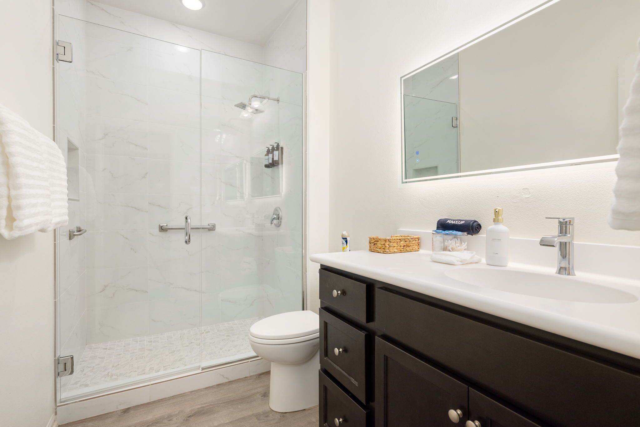 A modern bathroom with a glass-enclosed shower, a white toilet, and a vanity with a mirror and sink.