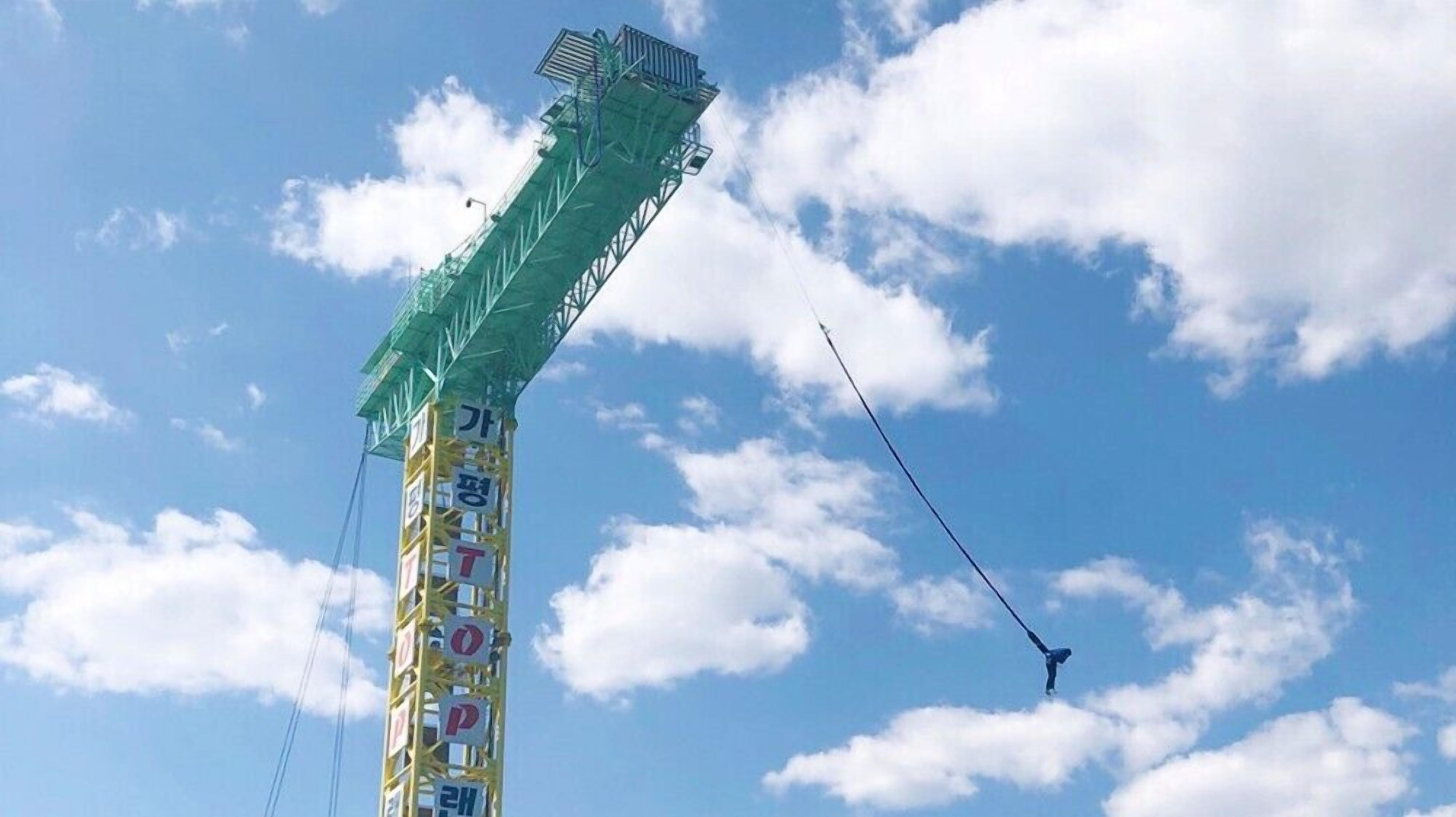 A tall structure with a green roof and multiple signs, including Korean characters, against a blue sky with clouds.
