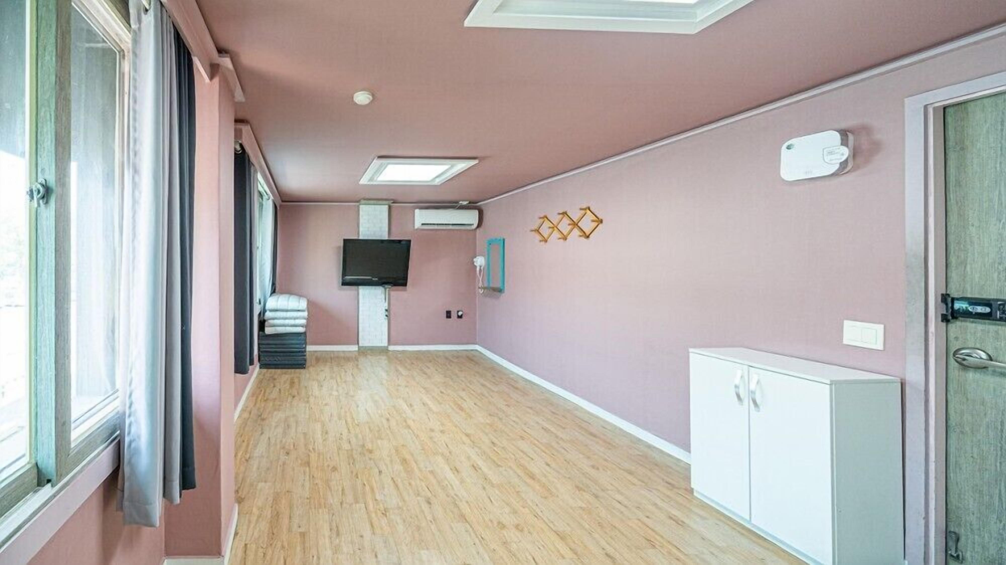 A hallway with a wooden floor, pink walls, a TV mounted on the wall, and a white cabinet on the right.