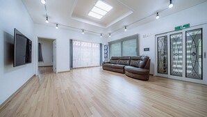 A spacious living room with a brown leather sofa, wooden flooring, a flat-screen TV mounted on the wall, and a skylight above. - the allin pension (Gapyeong)