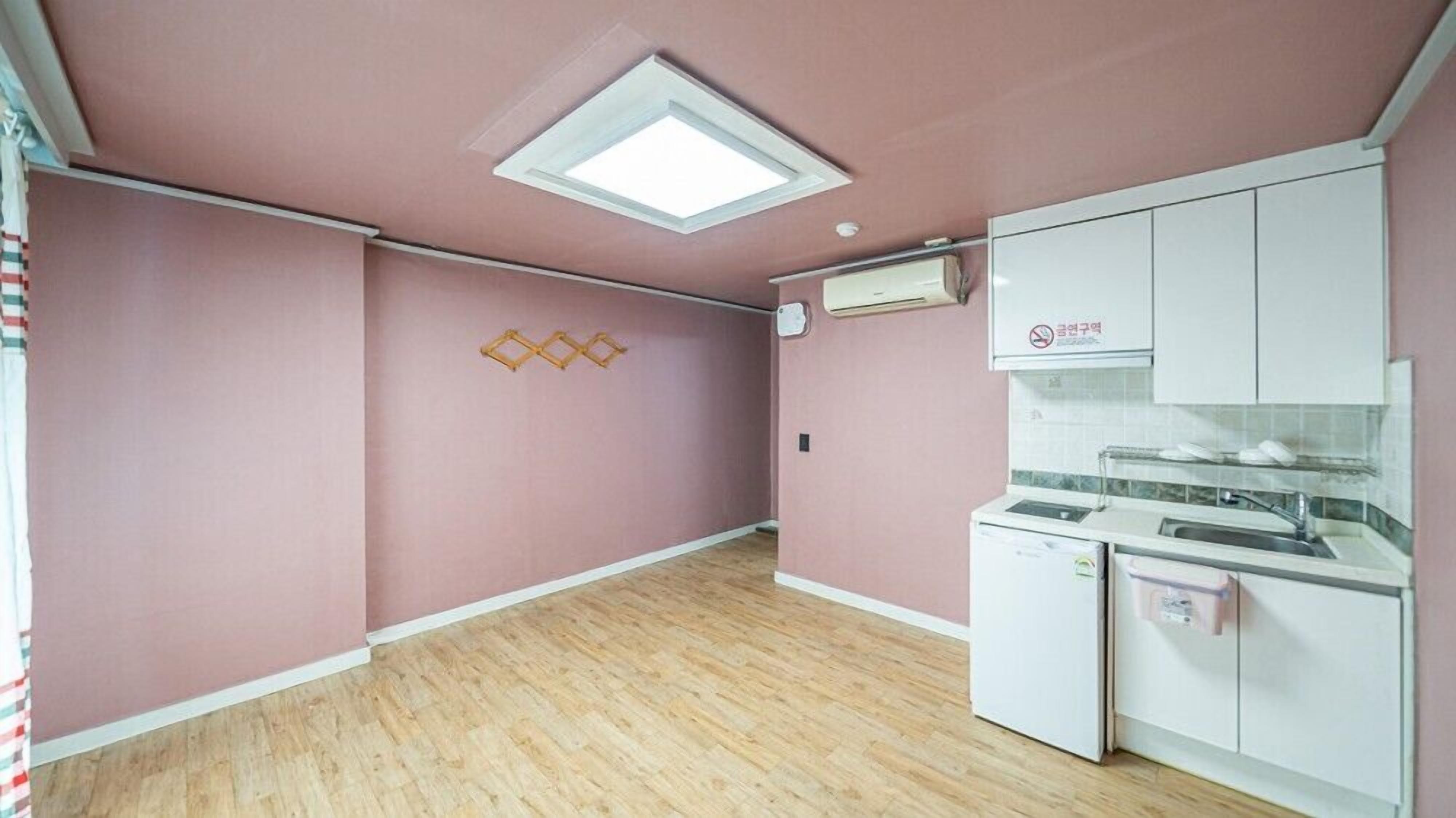 Et køkken med pink vægge, trægulv, ovenlys og hvide skabe.