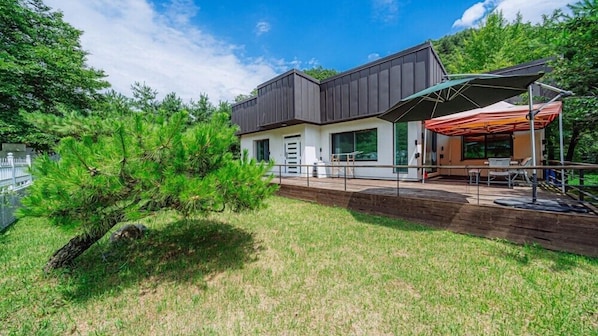 A modern building with a flat roof, large windows, and a covered outdoor seating area. - the allin pension (Gapyeong)