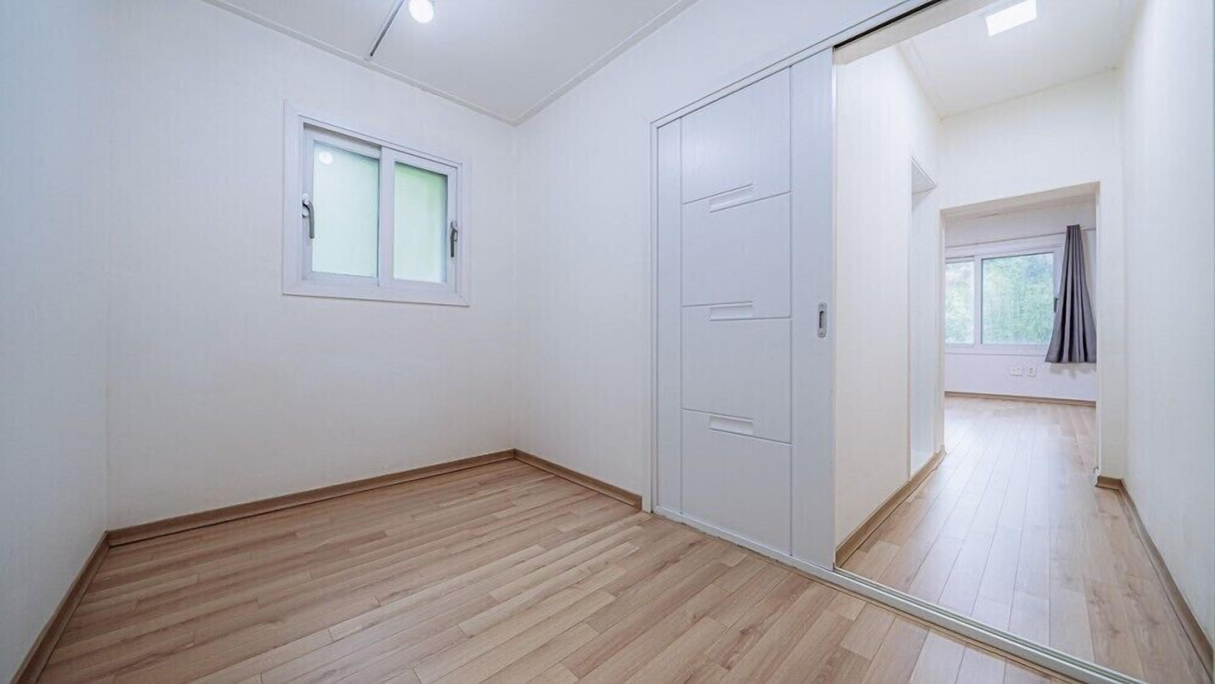 A room with wooden flooring, a white wardrobe, and a window with frosted glass.