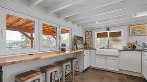 Una cocina moderna con armarios blancos, una encimera de madera y un amplio ventanal con vistas a un área boscosa.