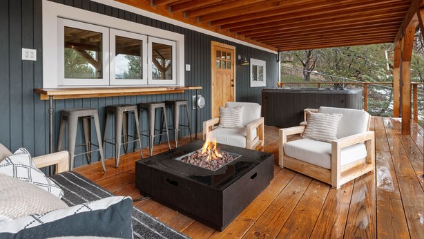 Un espacio al aire libre cubierto con una chimenea, taburetes de bar y dos sofás.