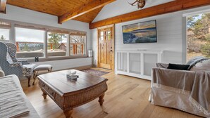 Un salón amplio con techo de madera, ventanas grandes, chimenea y vistas al exterior.