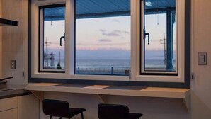 Cozinha moderna com uma janela ampla com vista para o mar, duas cadeiras pretas e bancada embutida.