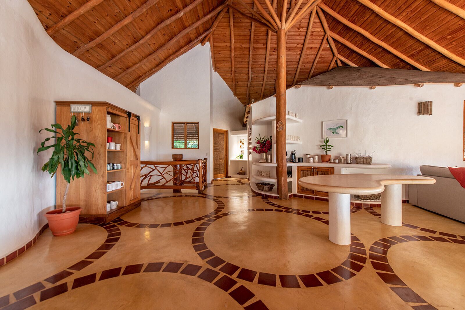 A spacious interior with a high wooden ceiling, a central round table, and a potted plant.