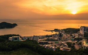 A coastal cityscape at sunset with buildings, a marina, and a hilly backdrop. - Beach Hill View House (Incheon)