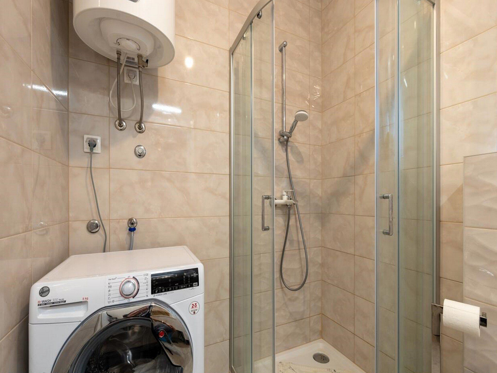 Un bagno compatto con doccia vetrata, lavatrice a muro e servizi igienici.