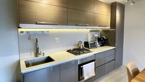 A modern kitchen with a built-in gas stove, stainless steel appliances, and a small dining area with a wooden table and chairs. - Trendy Chinatown apartment with parking (Vancouver)