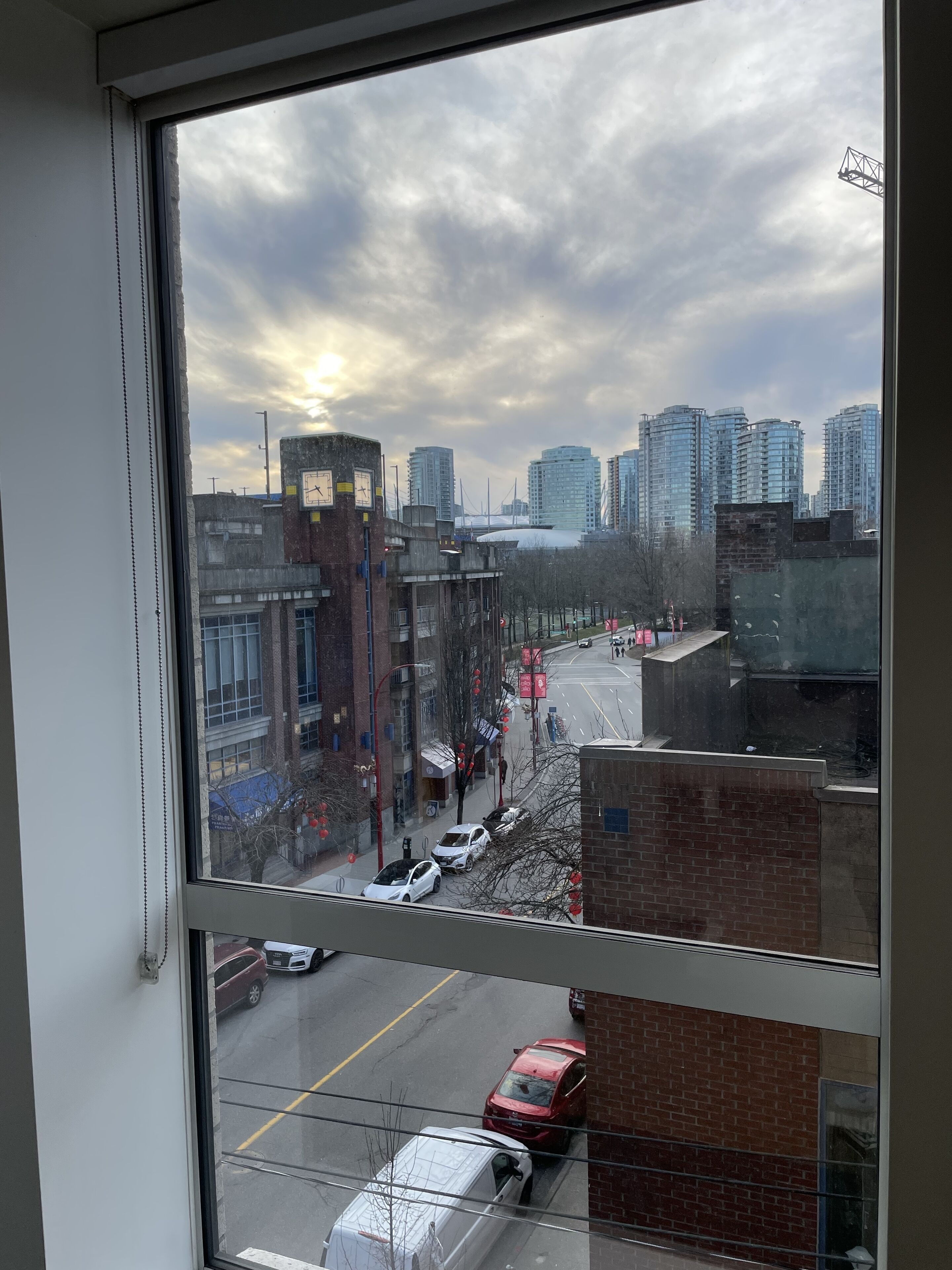 Vista urbana a través de una ventana, con edificios altos, una calle con automóviles y un cielo nublado.