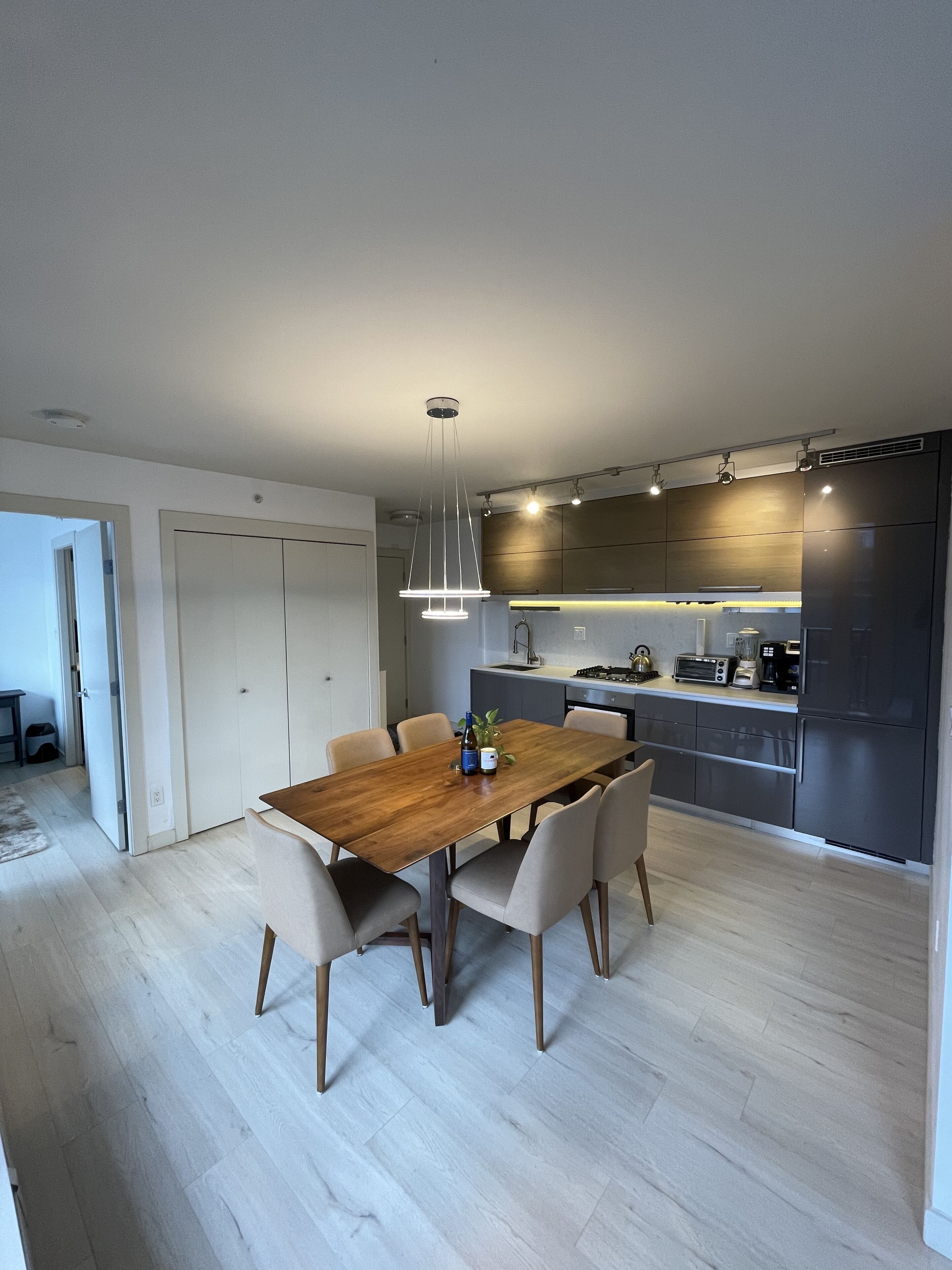 A modern kitchen with dark cabinetry, a wooden dining table, and a pendant light.