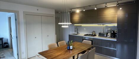A modern kitchen with dark cabinetry, a wooden dining table, and a pendant light.