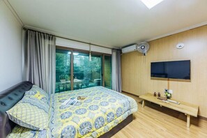 Un dormitorio con cama, televisor, banca y ventana con cortinas.