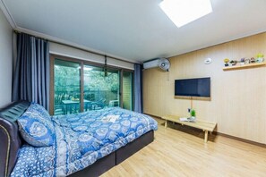 Un dormitorio con cama, televisor, ventana y una mesita.
