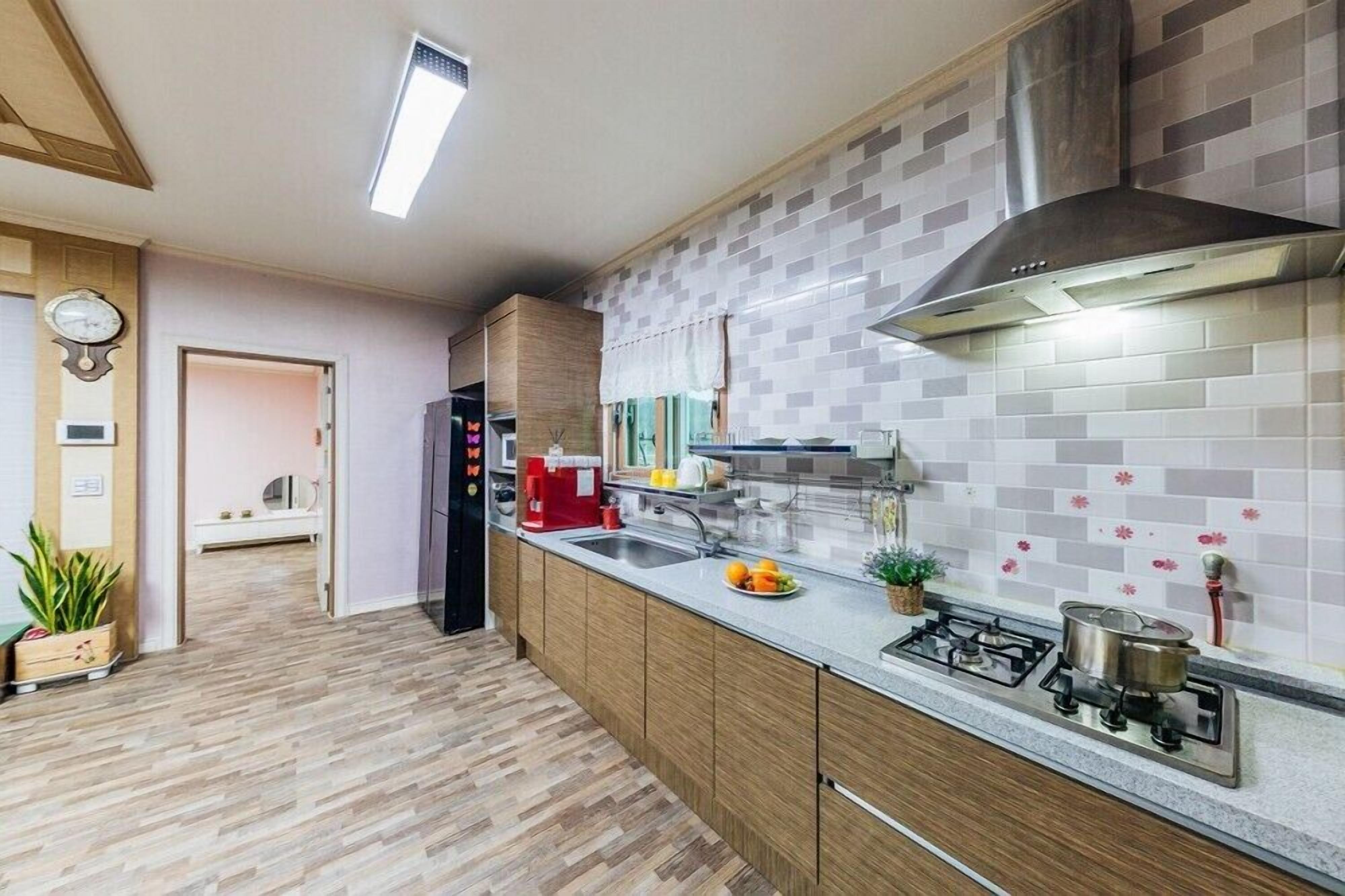 Une cuisine moderne équipée d’une cuisinière intégrée, d’un évier et d’une hotte en acier inoxydable. On y trouve également un meuble en bois et un plan de travail agrémenté d’une plante en pot.